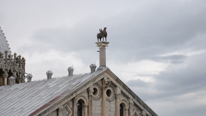 Atop a grand marble facade sits a metal griffin with wings.