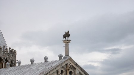 Atop a grand marble facade sits a metal griffin with wings.