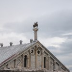 Atop a grand marble facade sits a metal griffin with wings.
