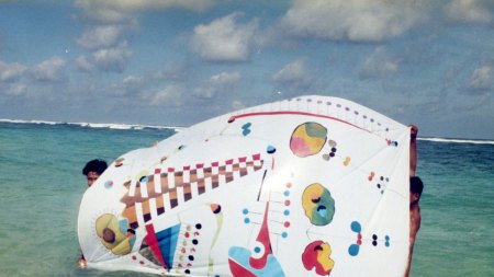 Two men hold up an unstretched canvas of an abstract painting in the water.