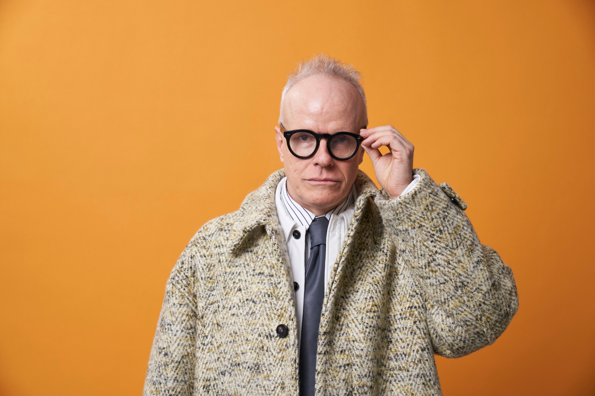 A white man in woolen jacket, black tie, and round black glasses.