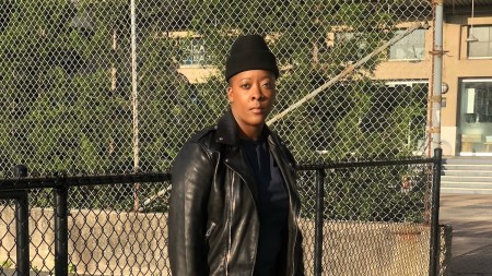 Black woman near a basketball court wearing a black leather jacket and jeans.