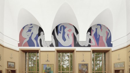 Under three archways, there's a painting of figures dancing by Matisse. Below that, in a gold painted room, are several paintings in gilded frames, but their subjects and details are not legible from far away.