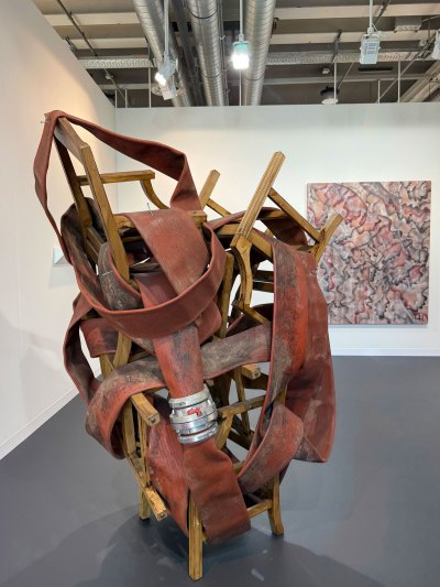 A sculpture in which a red fire hose is intertwined with various stacked wooden chairs.