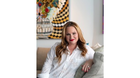 A woman in a white shirt lounging on a couch with a painting behind her.