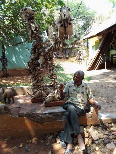 A man sits next to a sculpture made of various bone fragments. 