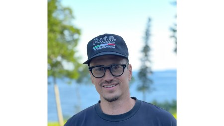 A portrait of man wearing glasses, a baseball cap, and a sweatshirt.
