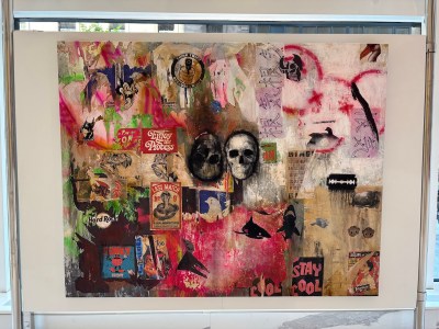 A painting of two skulls amid collaged labels and signs.