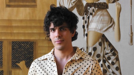 A portrait of a man with moppy black hair and a white polka-dotted shirt.