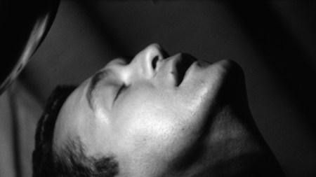 A black-and-white film still of a man with his head back, eyes closed, and mouth slightly ajar, as if relaxed or ecstacy.
