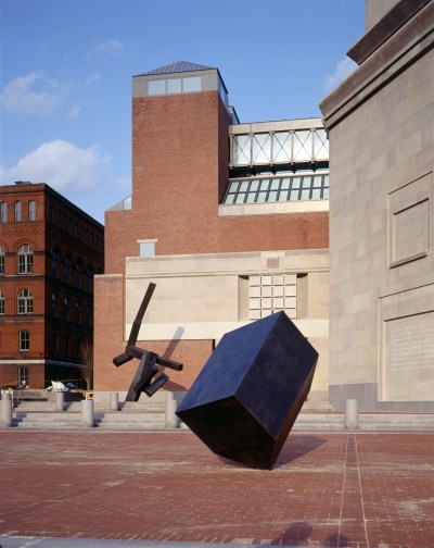 Two large black sculptures outside in front of a looming brick building.