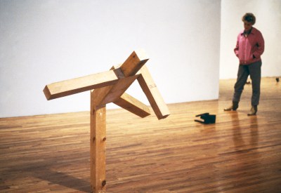 A person standing next to a sculpture of a figure bending over.