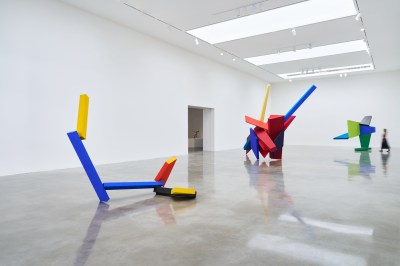 A large white gallery space with three multicolored planar sculptures standing on the floor.