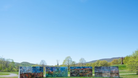 Four large sculptural slabs on green grass, with large metal sculptures rising in the background.