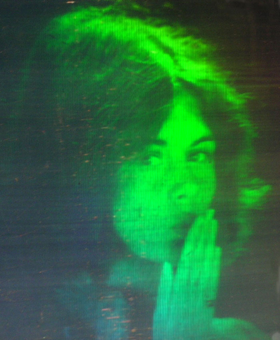 A hologram depicts a woman blowing a kiss, a 3D moving image rendered in shades of green