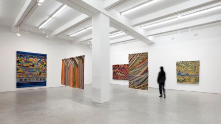A person walking through an exhibition of freestanding abstract weavings.