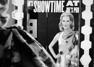 A black-and-white photo of a woman looking at herself in a vanity mirror.