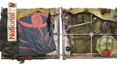 A sculpture featuring two pieces of metal fencing covered with fabrics and found objects including a saw.