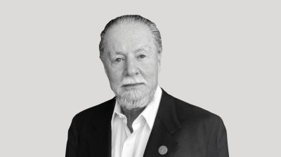 A silhouetted black-and-white portrait of an older white man with a beard in a suit on a gray background.