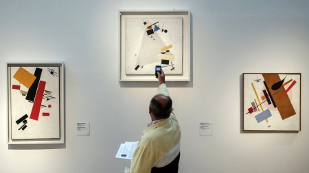 A man takes a photo of a painting on a wall.