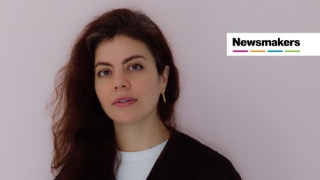 A woman with a black cardigan on looks at the camera. There is a badge in the top right that reads "Newsmakers."