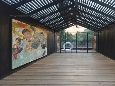 View of an abstract painting installed in the upstairs of a building with a white sculpture visible on a balcony in the background. 