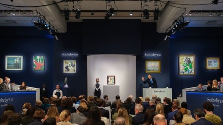 An auctioneer gestures before a crowded sales room.