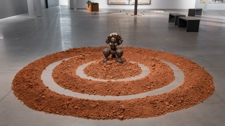 A sculpture of a feminine figure made of metal and encircled by orange clay.