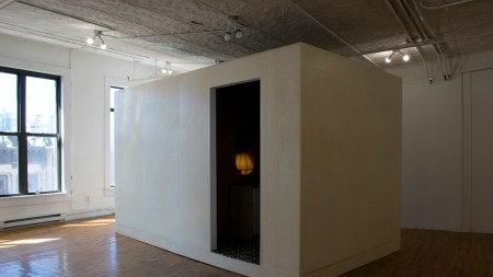Within an empty gallery stands a freestanding rectangular room with a dark interior.