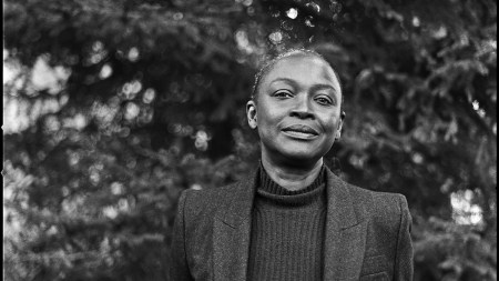 A black-and-white photograph of a Black woman in a vest standing amid trees.