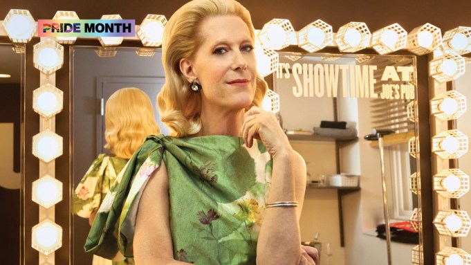 A blond woman in a green dress in front of a vanity mirror, backstage