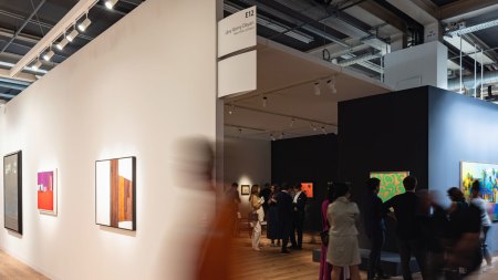 A long exposure photograph showing blurred figures navigating an art fair's booths.