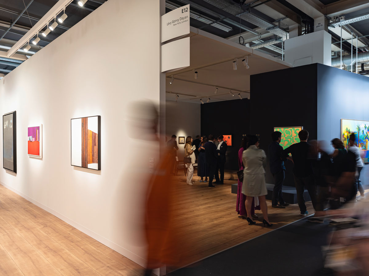 A long exposure photograph showing blurred figures navigating an art fair's booths.