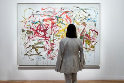 A woman in a gray suit and with a bob looks at an abstract painting by Joan Mitchell.