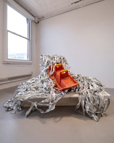 A sculpture made from a saddle-like structure with silvery plastic all around it.