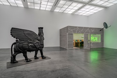 A sculpture of a black Assyrian lamassu next to a replica of an Iraqi internet cafe.