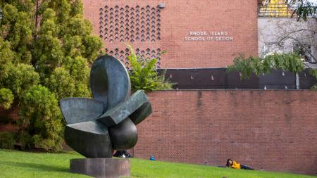 Students sit on a lawn next to a large sculpture on the campus at the Rhode Island School of Design.