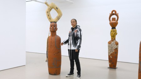 The artist standing between two sculptures of life-size human figures. in the forms of clay vessels.