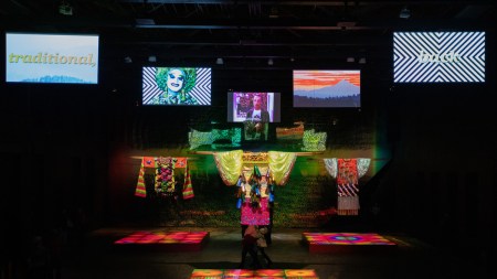 A cavernous space with five video screens and five oversize ceremonial garments hanging above three illuminated dance floors.