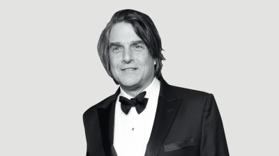 Black-and-white portrait of a young-looking, middle aged white man with long hair in a tuxedo