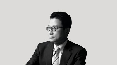 A silhouetted black-and-white portrait of an Asian man with glasses in a suit and tie on a gray background. He looks toward the left, away from the camera.
