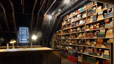 A stack of hundreds of boxes in an attick next to two tables equipped with reading lamps.