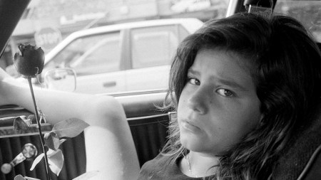A black-and-white photograph captures the artist's daughter holding a rose while sitting in a car with her leg out the window.