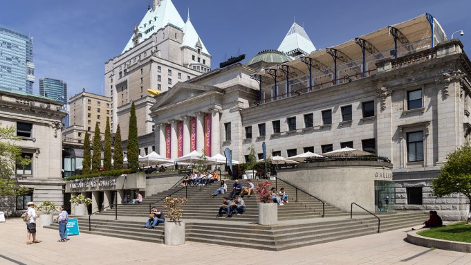 The front exterior of the Vancouver Art Gallery on a sunny day, showing several people sitting on its steps.