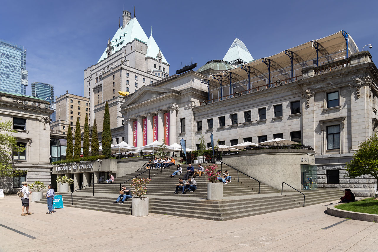 The front exterior of the Vancouver Art Gallery on a sunny day, showing several people sitting on its steps.