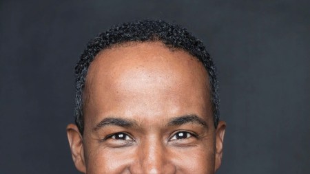 A portrait of a smiling Black man with a moustache.