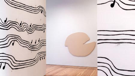 Two walls with musical notations on squiggly lines surround a beige round canvas that looks like two halves of a lumpy circle resting one on top of another.