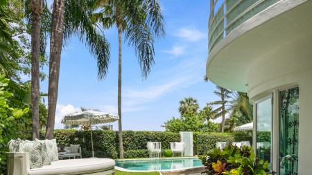 The facade of a home and a swimming pool surrounded by palm trees.