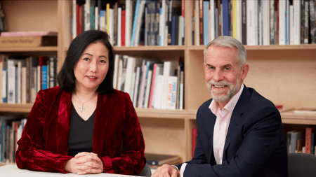 Man and woman sitting at table in front of book case.
